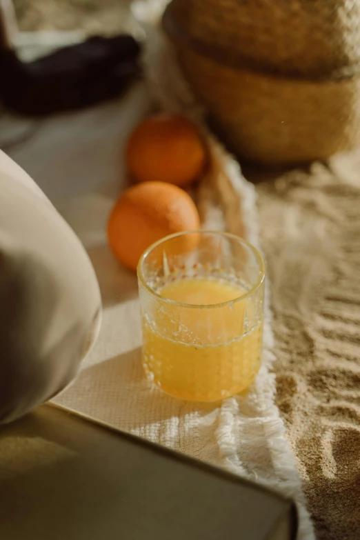 a glass of orange juice sitting on top of a table, a still life, by Nathalie Rattner, unsplash, linen, translucent eggs, moroccan, picnic