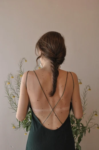 a woman standing in front of a vase of flowers, a tattoo, trending on pexels, bare back, sparse freckles, braided brown hair, ignant