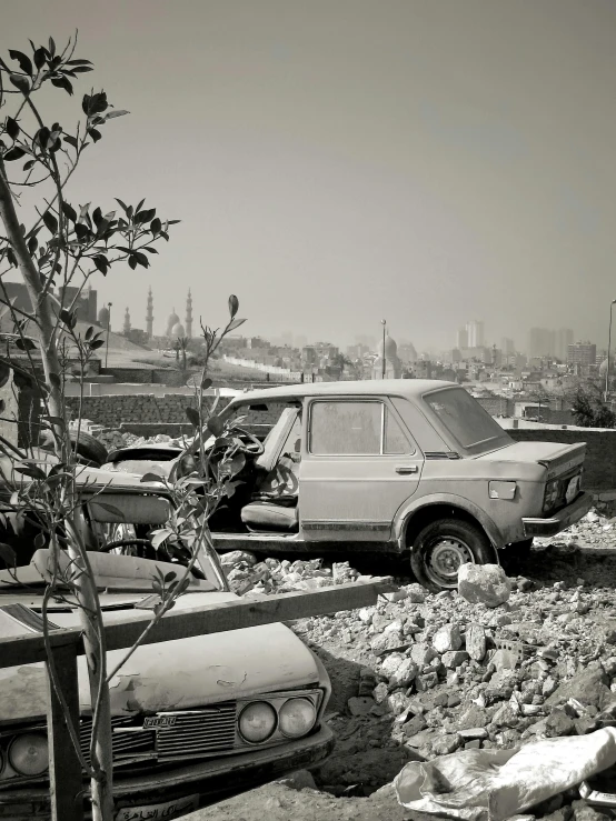 a bunch of cars that are sitting in the dirt, a black and white photo, inspired by Thomas Struth, conceptual art, posing in front of bombed city, hasan piker, ( ( photograph ) ), overlooking