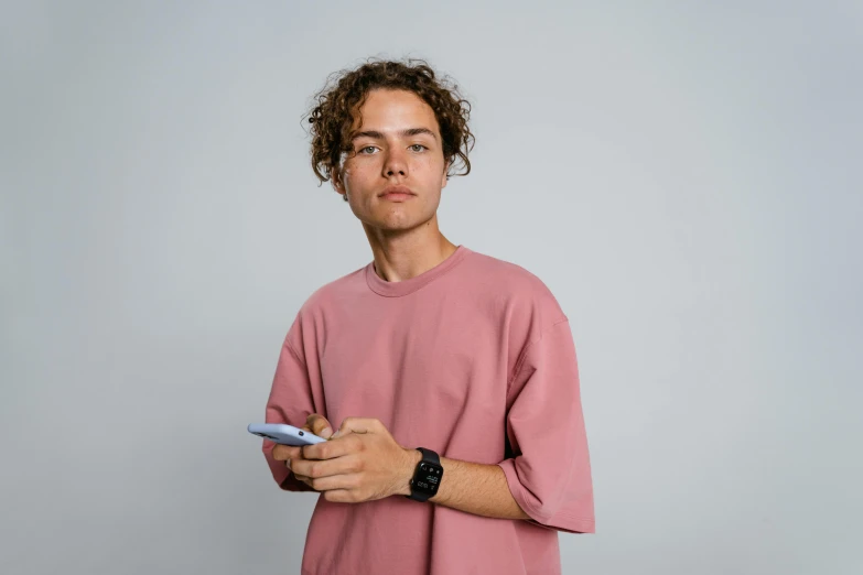 a man in a pink shirt holding a cell phone, a character portrait, trending on pexels, he has short curly brown hair, jovana rikalo, male teenager, stoic pose