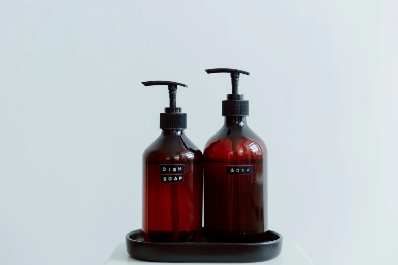 two bottles of liquid sit on a tray, unsplash, purism, soap, japanese collection product, dark red, full body image