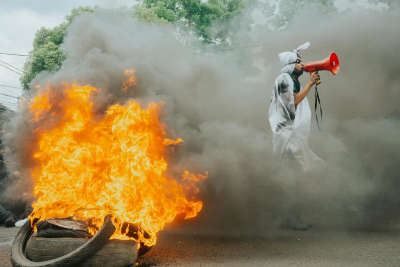 a man holding a megaphone in front of a fire, by Julia Pishtar, pexels contest winner, conceptual art, one single man in a hazmat suit, violent protest, off - white collection, photograph of the year