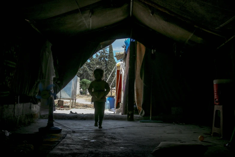 a person standing inside of a tent in the dark, hurufiyya, walking boy, inside a shed, seen from afar, an olive skinned