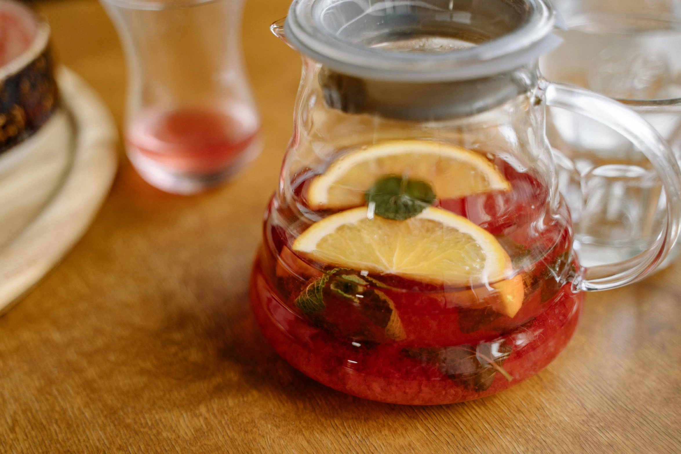 a pitcher filled with fruit sitting on top of a wooden table, ice cubes, charli bowater, thumbnail, hibiscus