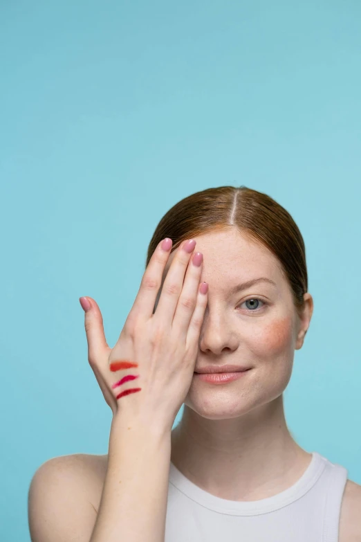 a woman covering her eyes with her hands, by Julia Pishtar, trending on pexels, renaissance, red birthmark, with a blue background, ellie bamber, red facial stripe