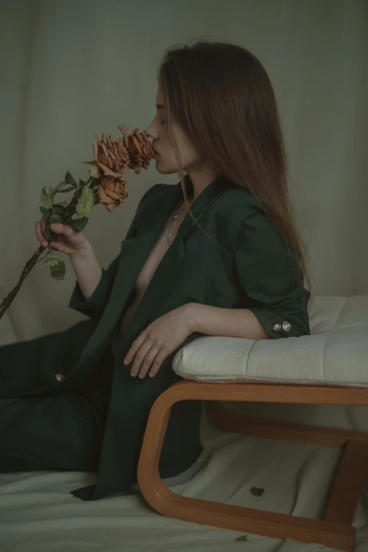 a woman sitting on a bed holding a flower, inspired by Elsa Bleda, pexels contest winner, aestheticism, wearing green suit, profile image, roses, sitting in a lounge
