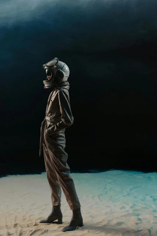 a man standing on top of a sandy beach, a surrealist sculpture, inspired by Gottfried Helnwein, unsplash, in a space cadet outfit, dark studio backdrop, wearing flight suit, oil on canvas. cinematic