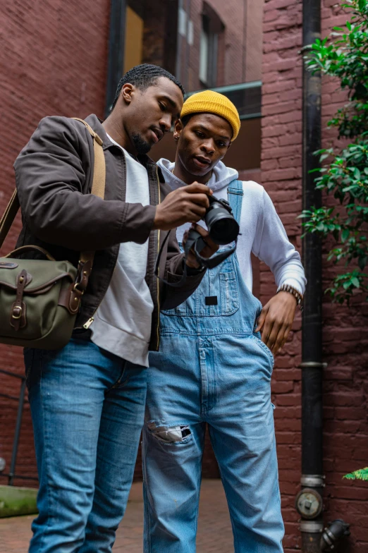 a couple of men standing next to each other, a picture, trending on pexels, holding a camera, harlem, overalls, color photo