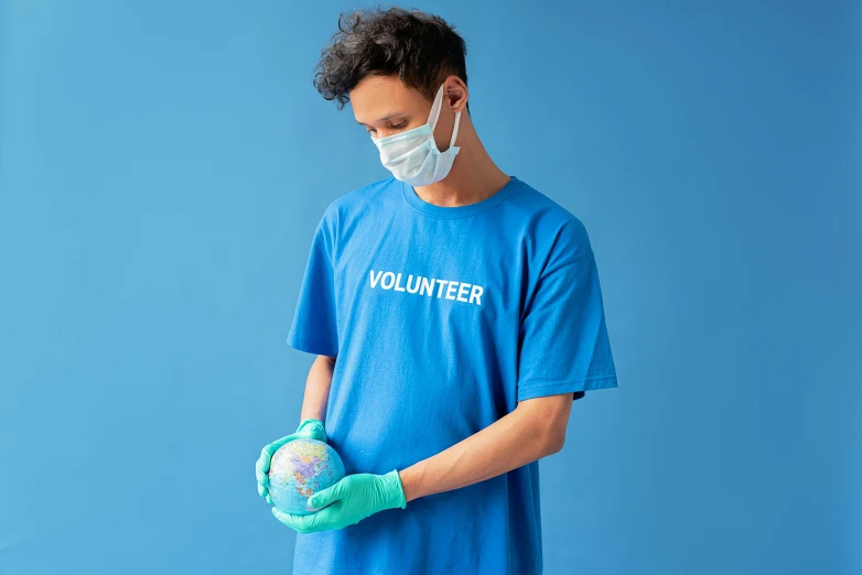 a man in a blue shirt holding a soccer ball, by Francis Helps, pexels contest winner, healthcare worker, dust mask, violet coloured t-shirt, globes