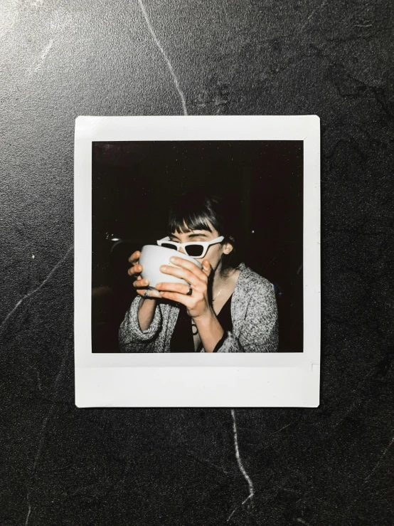 a person taking a picture with a camera, a polaroid photo, inspired by Elsa Bleda, trending on pexels, an alien drinking horchata, black and white color only, declan mckenna, wearing black frame glasses