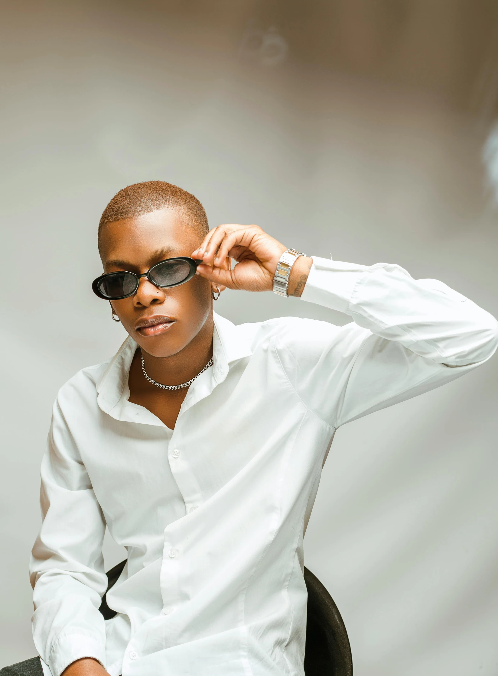 a man in a white shirt and sunglasses sitting on a chair, by Lily Delissa Joseph, androgynous person, brown buzzcut, kano), high quality photo