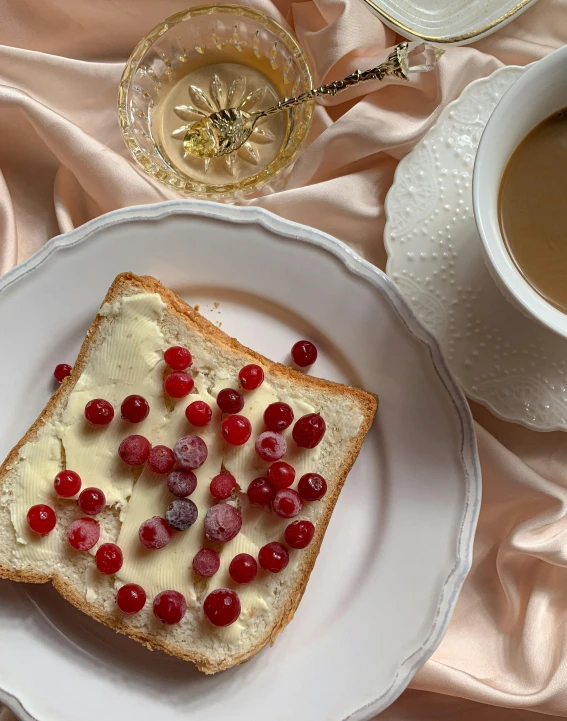 a white plate topped with a piece of bread next to a cup of coffee, a still life, trending on instagram, art nouveau, submerged in cranberries, thumbnail, 🎀 🧟 🍓 🧚, creamy skin