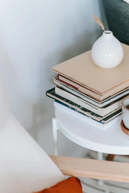 a white vase sitting on top of a table next to a stack of books, white sheets, detailed product image, multiple stories, morning coffee