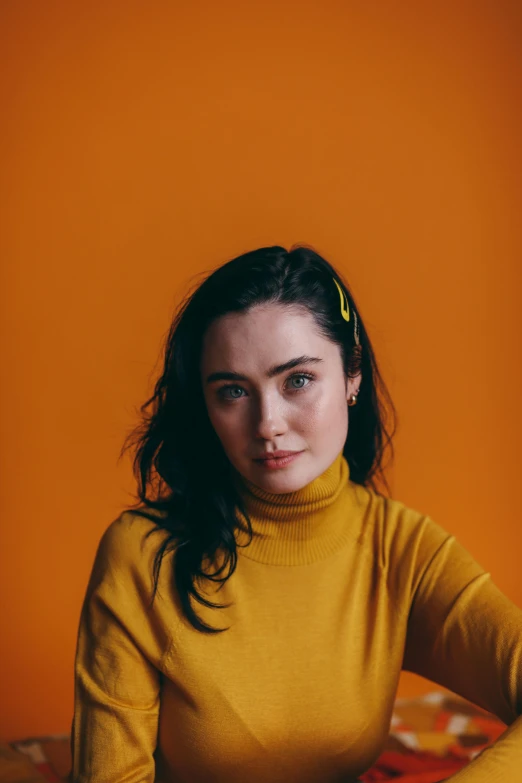 a woman sitting at a table with a plate of food, an album cover, pexels contest winner, maisie williams, in front of an orange background, wearing turtleneck, yellow hue