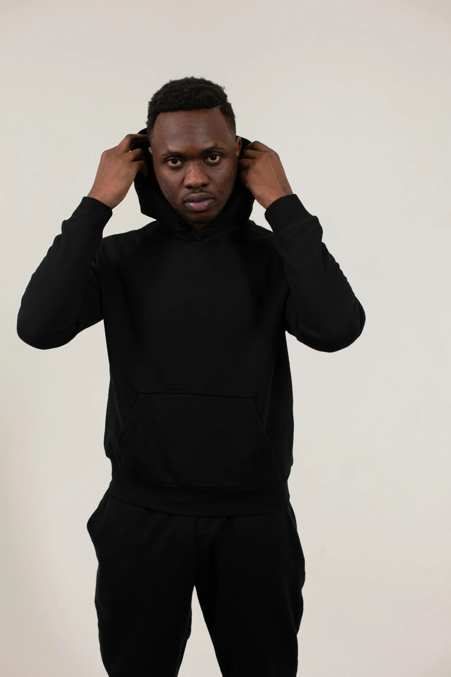 a man in a black hoodie standing with his hands on his head, curated collections, main colour - black, front, david uzochukwu