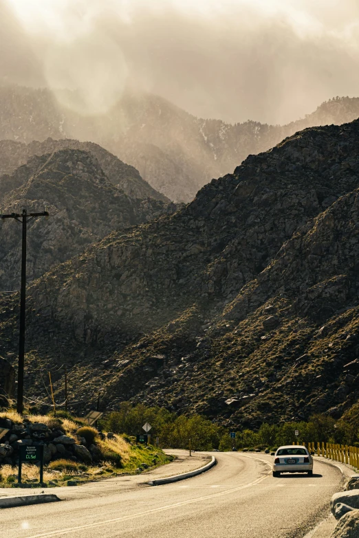a car driving down a road with mountains in the background, by Jeffrey Smith, unsplash contest winner, modernism, telephone wires, palm springs, geological strata, late afternoon light
