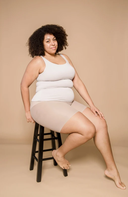 a woman in a white tank top sitting on a stool, plus-sized, tights skin, 15081959 21121991 01012000 4k, tan skin a tee shirt and shorts