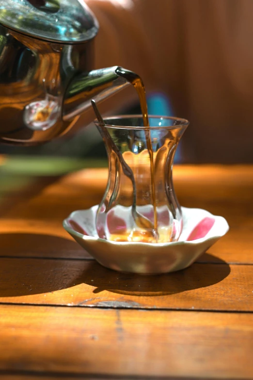 a tea pot pouring tea into a cup, hurufiyya, on a wooden table, photograph taken in 2 0 2 0, turkey, flowing