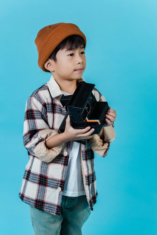 a young boy wearing a hat and holding a camera, inspired by Reuben Tam, unsplash, visual art, tartan garment, slide show, studio medium format photograph, toys
