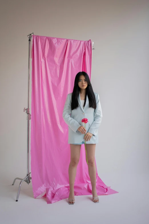 a woman standing in front of a pink backdrop, an album cover, inspired by Russell Dongjun Lu, wearing a light blue suit, in a photo studio, a young asian woman, fully covered in drapes