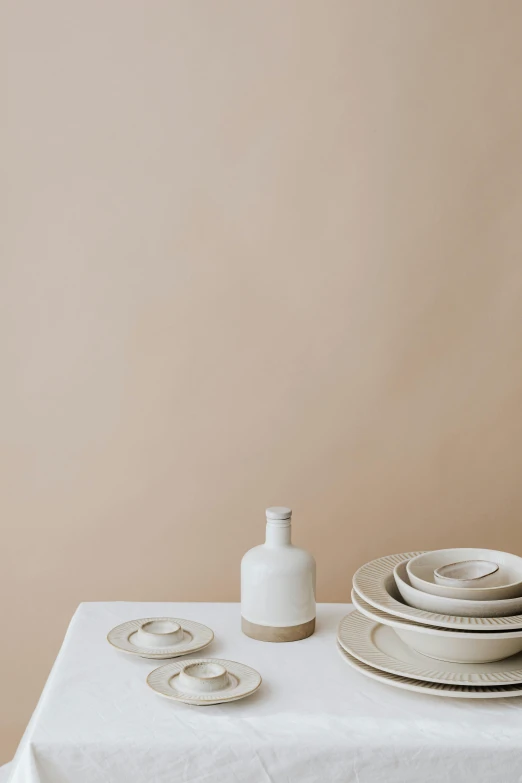 a white table topped with plates and bowls, a still life, trending on unsplash, minimalism, sandy beige, white wine bottle, two tone, studio backdrop