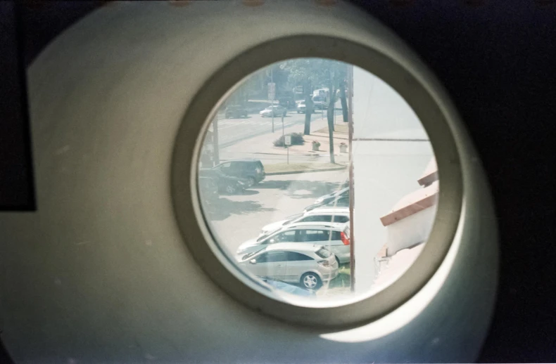 a view of a parking lot through a round window, a polaroid photo, inspired by André Kertész, unsplash, photorealism, parked spaceships, security cam, disposable camera, inside of a car