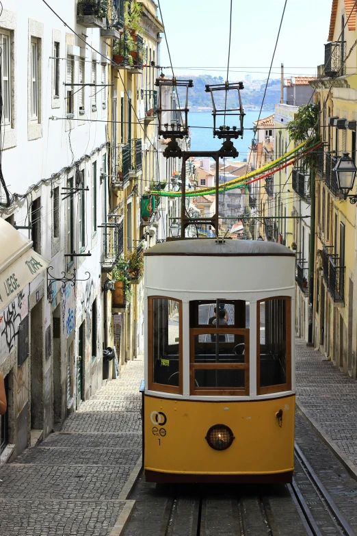 a yellow and white trolley traveling down a narrow street, inspired by Almada Negreiros, flickr, overlooking, square, tan, preserved historical