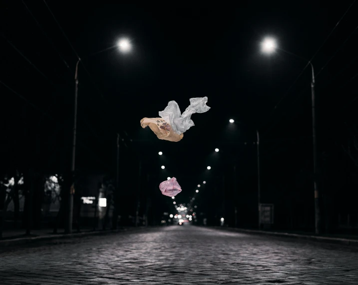 a person doing a trick on a skateboard in the air, an album cover, pexels contest winner, street art, floating lanterns, dressed in plastic bags, night photo, white and pink cloth