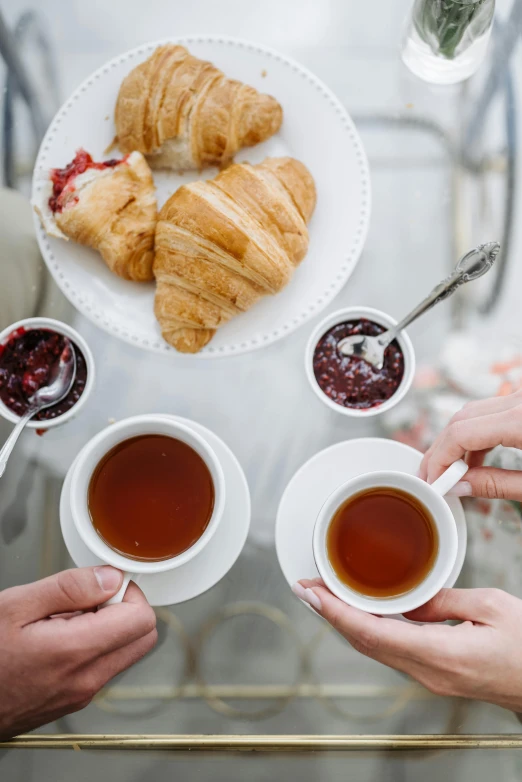 a group of people sitting at a table with cups of tea and croissants, a still life, trending on pexels, half image, sparkling, high quality photo, high angle shot