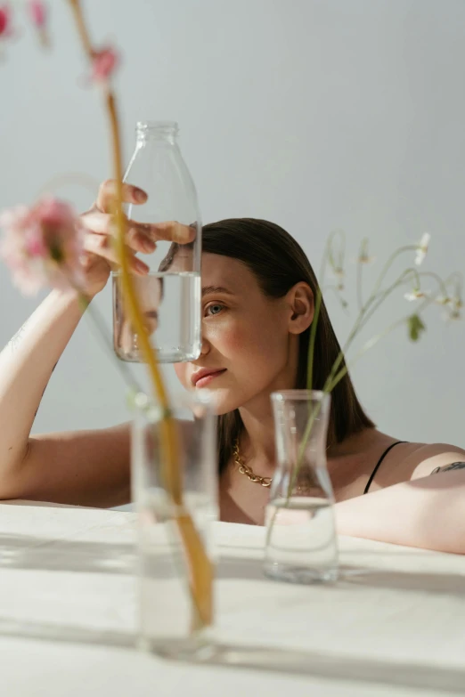 a woman sitting at a table with a vase of flowers, trending on pexels, renaissance, tansparent water, product shoot, fine simple delicate structure, bottle