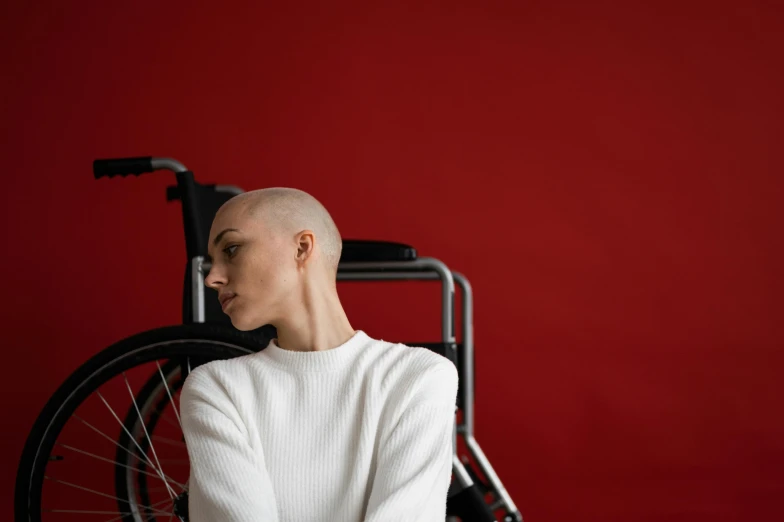 a man sitting in a wheel chair in front of a red wall, a portrait, by Emma Andijewska, pexels contest winner, antipodeans, buzz cut hair, young female, 15081959 21121991 01012000 4k, sickness