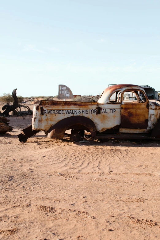 a rusted out truck sitting in the middle of a desert, old signs, burned cars, shipwreck, tombstone