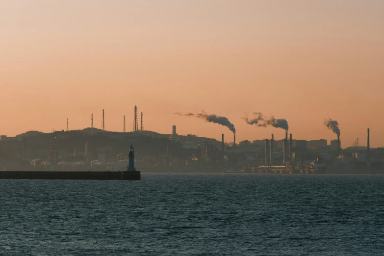 a large body of water with a lot of smoke coming out of it, pexels contest winner, harbour in background, in a sunset haze, sustainable materials, metal towers and sewers