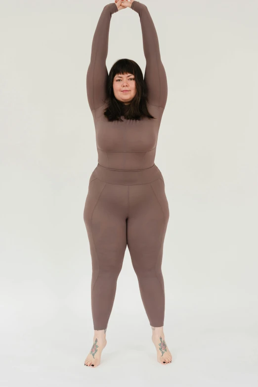 a woman standing with her arms in the air, inspired by Weiwei, muted colored bodysuit, obese, taupe, wearing a track suit