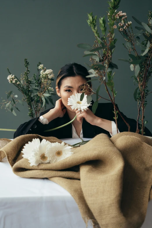 a woman sitting at a table with flowers in front of her, inspired by Kim Tschang Yeul, minimalism, high - end fashion photoshoot, linen, set on singaporean aesthetic, doing an elegant pose over you