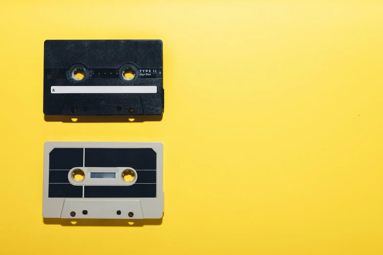 two cassettes sitting next to each other on a yellow surface, trending on pexels, lined up horizontally, black an white, high samples, from 1985