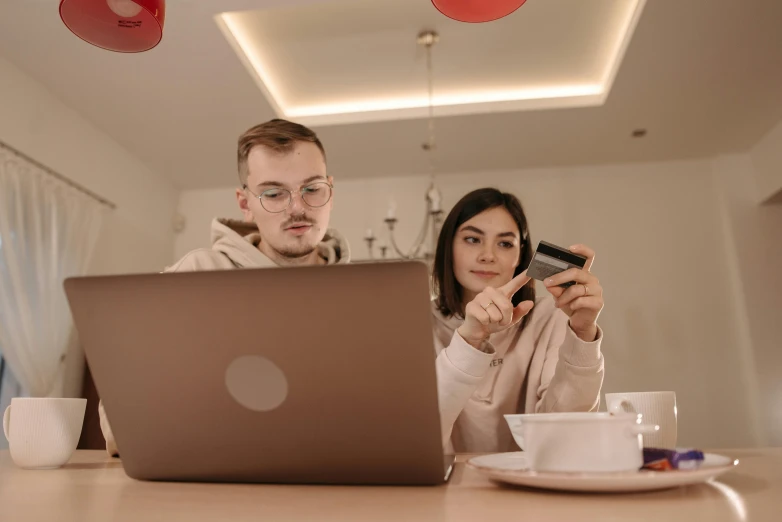 a man and a woman sitting at a table looking at a laptop, by Adam Marczyński, pexels contest winner, people shopping, avatar image, performing, looking at camera