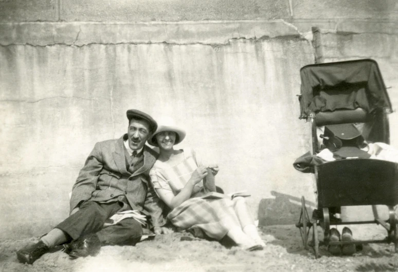 a man and woman sitting next to a baby carriage, a black and white photo, by Algernon Talmage, art nouveau, before a stucco wall, having fun in the sun, british pathe archive, selfie photo