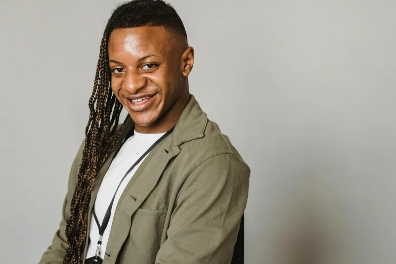 a man with dreadlocks sitting in a chair, inspired by Lawrence Harris, trending on pexels, smiling and looking directly, androgynous male, in front of white back drop, a man wearing a black jacket
