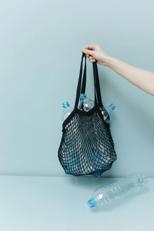 a woman holding a mesh bag filled with water bottles, pexels contest winner, black and teal paper, environment, minimalistic design, fishnets