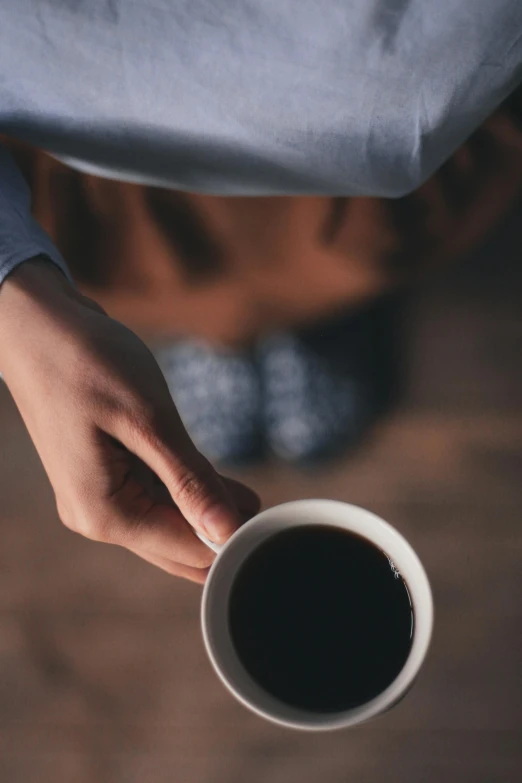 a person holding a cup of coffee, head down, dark hues, uncrop, sleepy