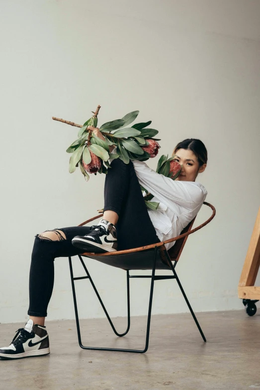 a woman sitting in a chair holding a plant, she is wearing streetwear, exploding roses, sydney sweeney, studio