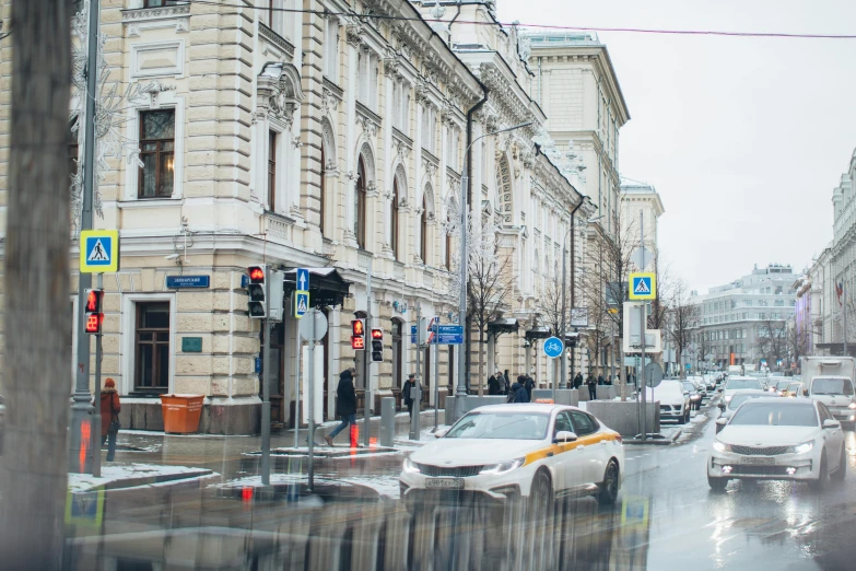 a city street filled with lots of traffic next to tall buildings, by Julia Pishtar, pexels contest winner, socialist realism, winter storm, russian neoclassicism, white building, wet pavement