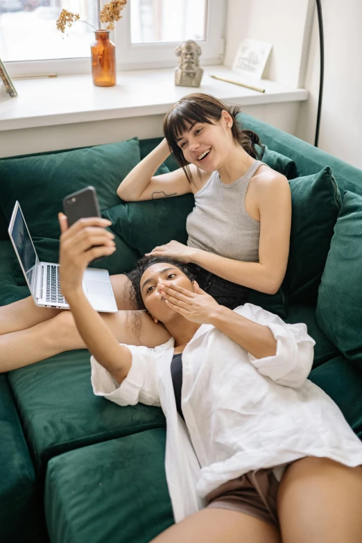 a man and a woman sitting on a green couch, a picture, trending on pexels, happening, taking a selfie, asian women, lesbian, sisters