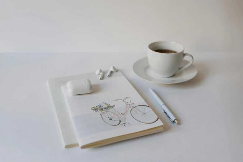 a notepad sitting on top of a table next to a cup of coffee, a drawing, bicycles, white background, porcelain organic tissue, plain background