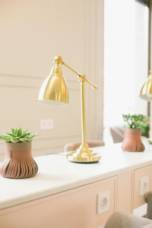 a white desk topped with a lamp next to a window, inspired by Constantin Hansen, trending on unsplash, gold decorations, detailed product image, accented in bright metallic gold, professional product photo