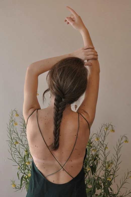 a woman standing in front of a vase of flowers, a tattoo, by Sara Saftleven, trending on pexels, long braided hair pulled back, yoga pose, wearing a camisole, hair : long brown