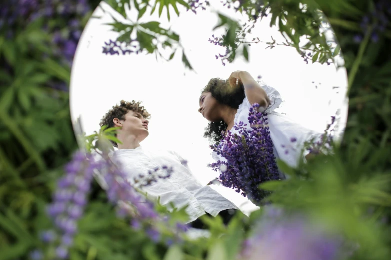 a man and a woman standing in front of a mirror, an album cover, unsplash, romanticism, lilac bushes, shot from below, gardening, white and purple