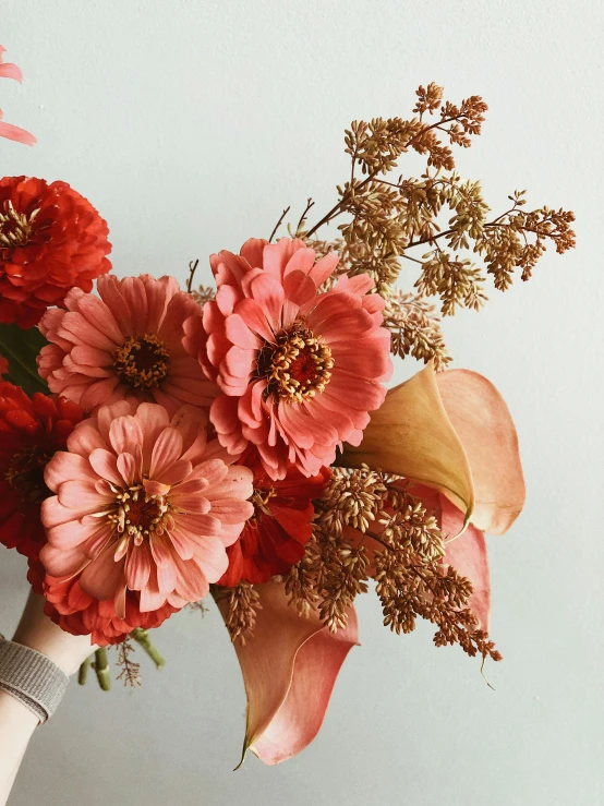 a bouquet of flowers in a vase on a table, light red and deep orange mood, in style of britt marling, holding flowers, gold flaked flowers