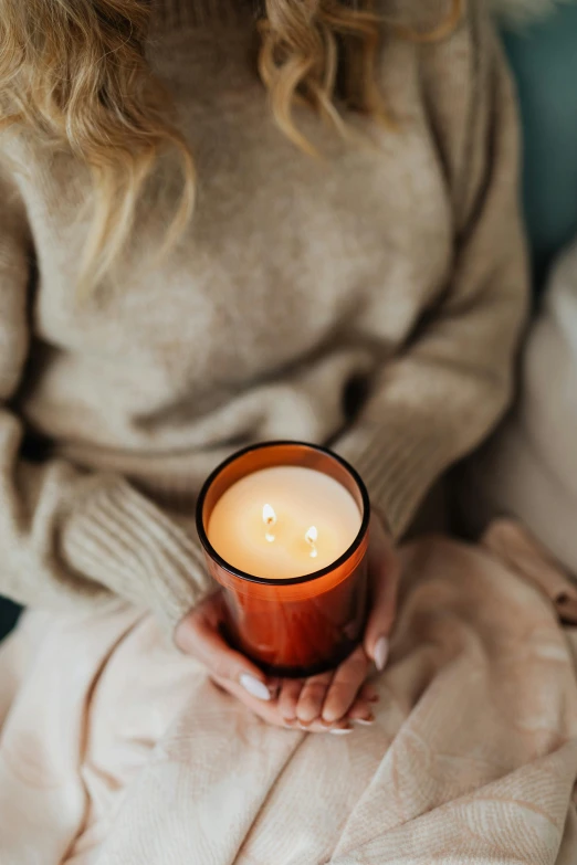 a woman sitting on a couch holding a candle, light orange mist, crimson, made of glazed, amber